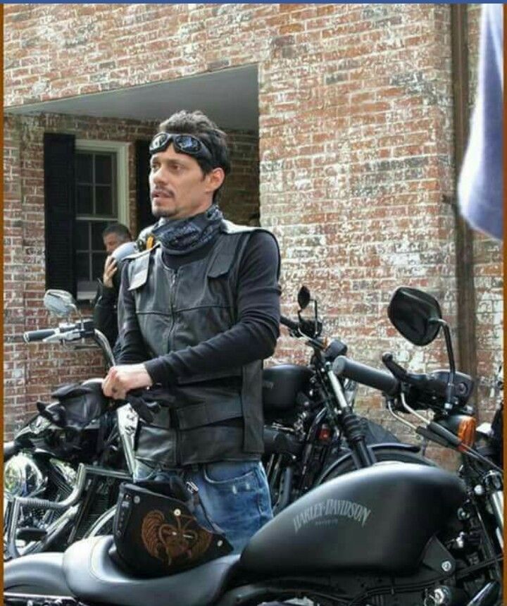 a man standing next to his motorcycle in front of a brick building with an american flag