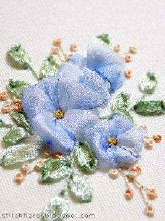 two blue flowers with green leaves on a white cloth background and beaded pearls around the edges