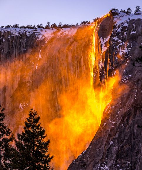 an image of a waterfall that is glowing in the night sky with trees around it