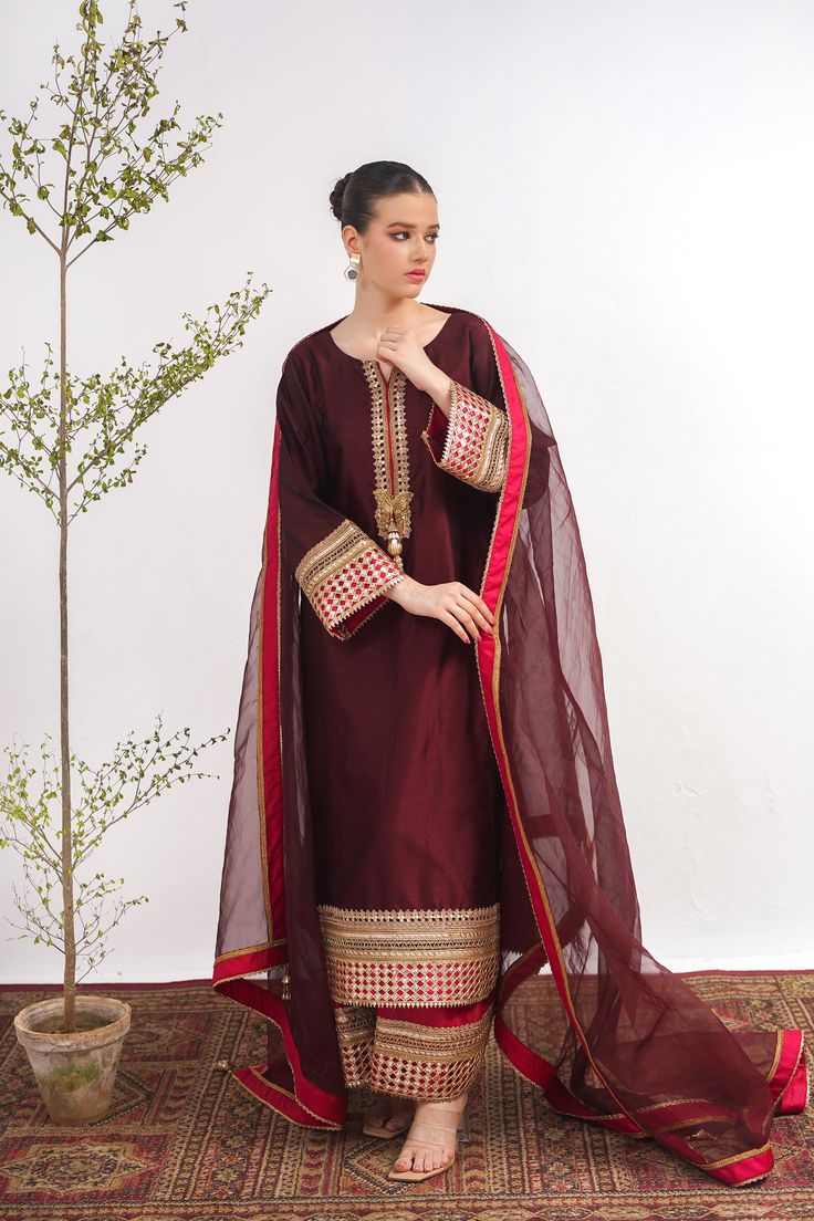 A maroon, raw silk, Kashmiri cut long kurta with Marori lace on the neck and sleeves. A pink tissue silk ajar pant lends a royal look to the suit. Finished with a matching tissue organza dupatta with pink border. 3-piece suit Ready to wear Formal Silk Salwar Kameez With Sheer Dupatta, Anarkali Tissue Silk Dupatta For Formal Occasions, Formal Organza Traditional Wear With Dabka, Formal Anarkali Tissue Silk Dupatta, Luxury Designer Tissue Silk Churidar, Semi-stitched Formal Kurta With Sheer Dupatta, Formal Organza Salwar Kameez With Dabka Detail, Formal Semi-stitched Kurta With Sheer Dupatta, Formal Cotton Silk Anarkali Set With Resham Embroidery