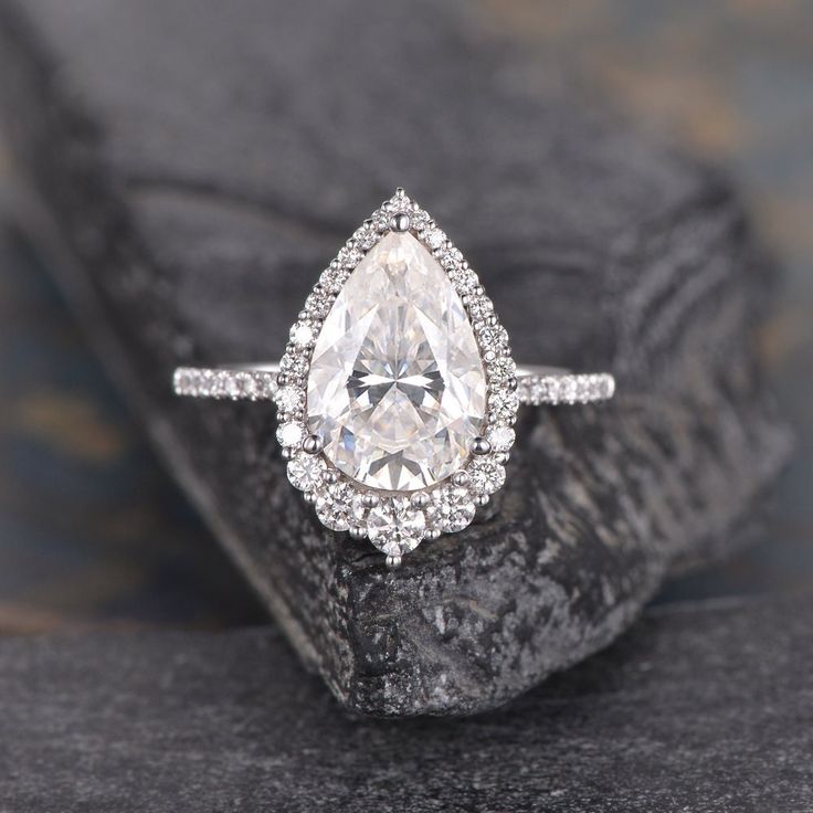 an engagement ring with a pear shaped diamond surrounded by small round diamonds on a rock