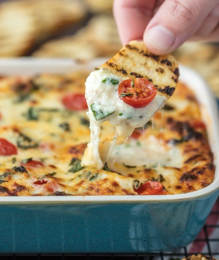 a piece of pizza being lifted from a casserole dish with cheese and tomatoes