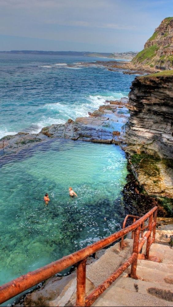 two people swimming in the ocean next to some rocks and water with stairs leading up to them