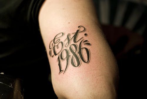 a man with a tattoo on his arm that reads est 80, and has the date in cursive writing