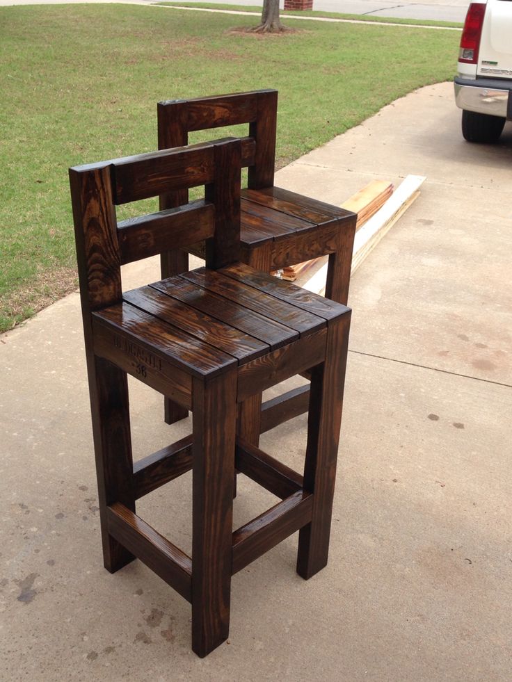 a wooden chair sitting on top of a sidewalk next to a white car and grass