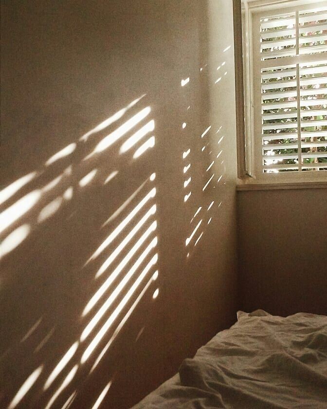 the sun is shining through the window blinds in this small room with white bedding