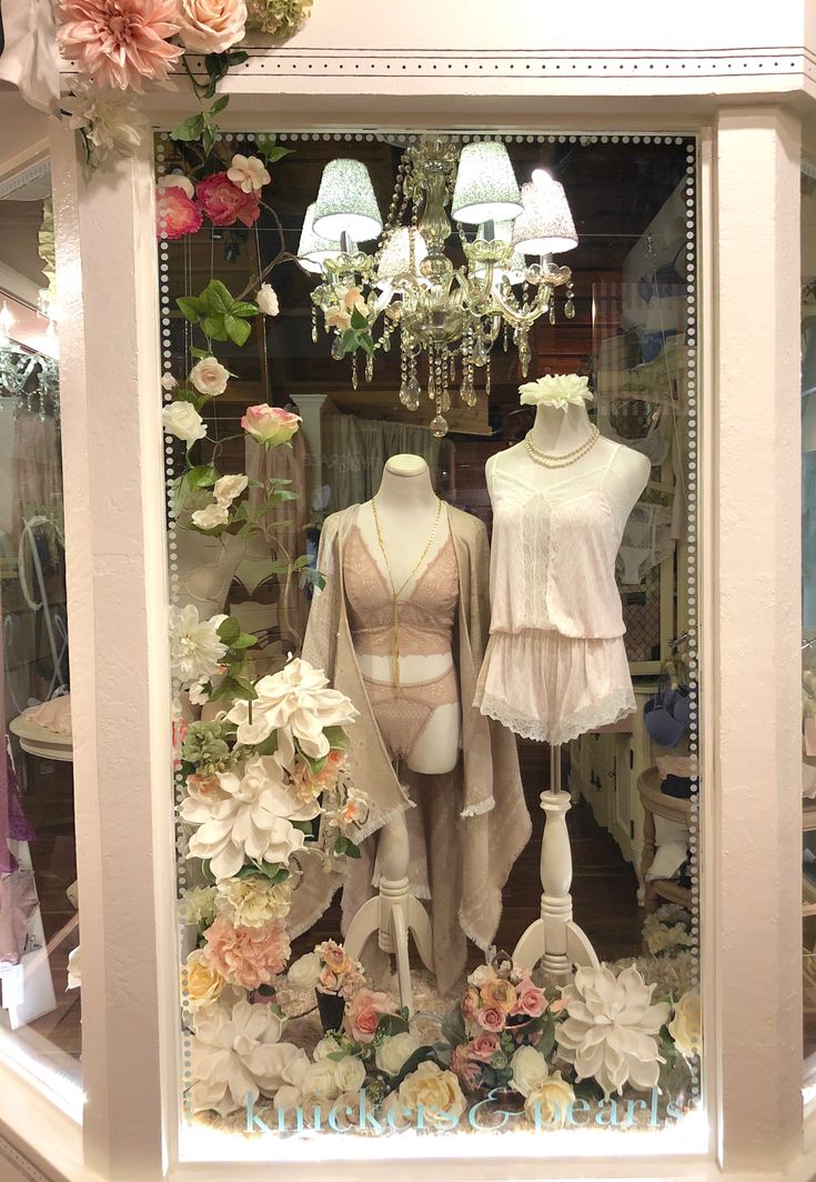 two mannequins in a display case with flowers and chandeliers