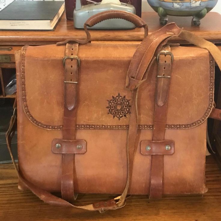 This very vintage leather bag is an artisan piece, with provenance in East Tennessee.  The detail here is excellent, with naturally tanned leather, buckles and satchel style binding straps.  Broad hand lacing details at the side were used to layer double side panels, giving the bag amazing stability.  There are 3 divided sections and a couple of slip pockets on the inside, the dividers are also in the lacing. This comes from the era of craft fairs that were most prevalent in the 60's and 70's. The hippy, and arts and crafts influences are so obvious here.  Imagine finding this at an outdoor booth at the Ramps Festival of Cosby or maybe from a vendor that traveled to the Dogwood Arts Festival in Knoxville.  Then imagine carrying this bag to your next Renaissance Fair or to your office.  It Vintage Leather Backpack With Leather Lining, Vintage Leather Shoulder Backpack For Travel, Vintage Brown Leather Backpack For Everyday, Vintage Rectangular Leather Backpack, Vintage Rectangular Leather Backpack For Daily Use, Vintage Brown Leather Satchel Backpack, Traditional Hand Tooled Satchel For Travel, Traditional Hand-tooled Satchel For Travel, Vintage Leather Satchel Backpack For Everyday