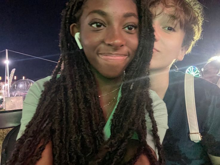 two women sitting next to each other in front of an amusement park at night time