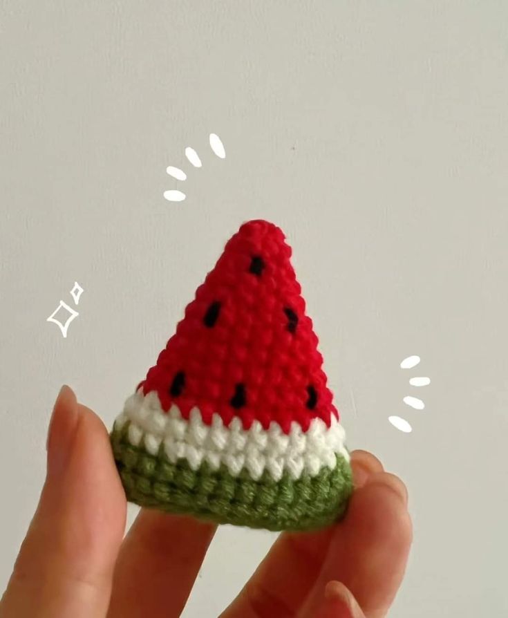 a hand is holding a small crocheted watermelon slice