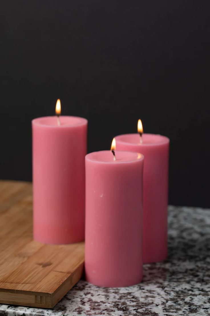 three pink candles sitting on top of a wooden cutting board