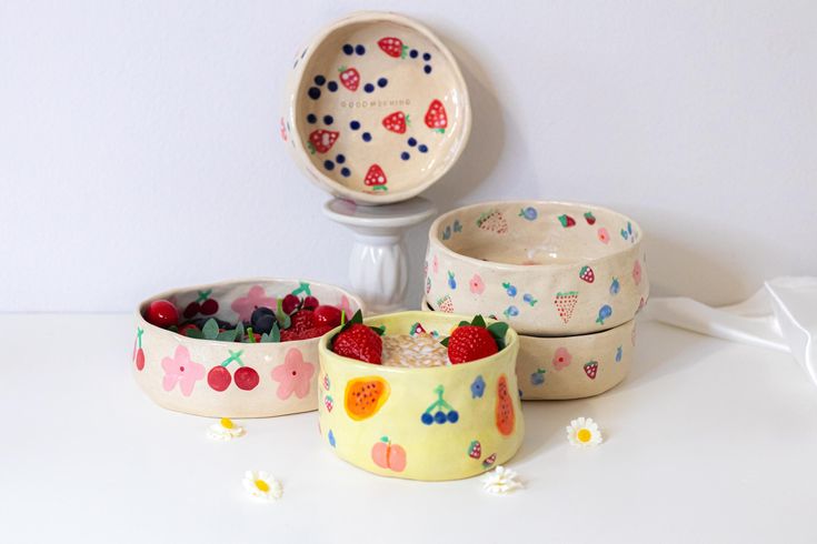 four bowls with fruit painted on them are sitting next to a white wall and an object in the background