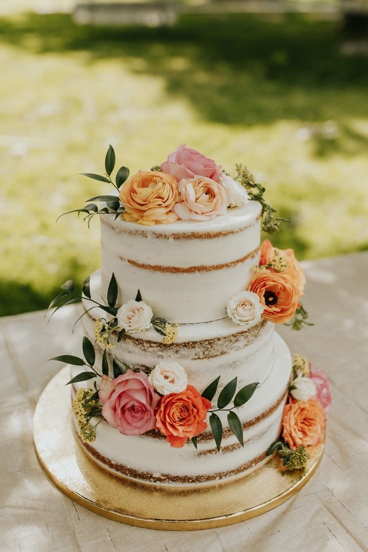 a three tiered wedding cake with flowers on the top and bottom is sitting on a table outside