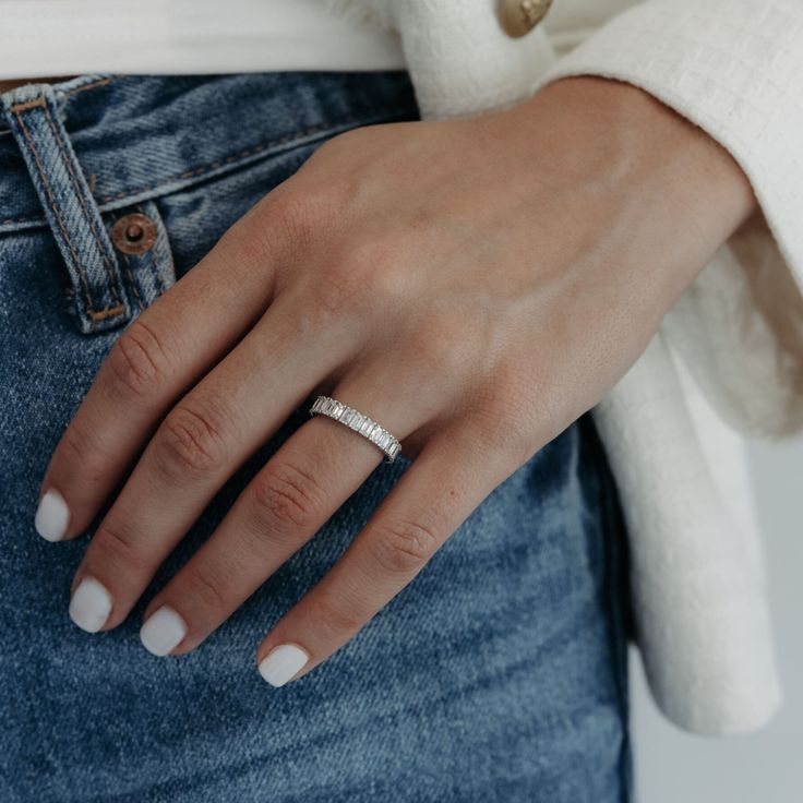 a woman's hand with a ring on her finger and white nails, wearing jeans