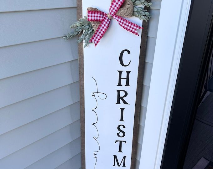 a christmas sign hanging on the side of a house with a red and white bow