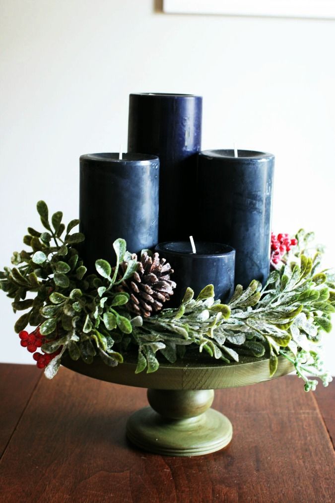 three black candles sitting on top of a green bowl filled with greenery and pine cones