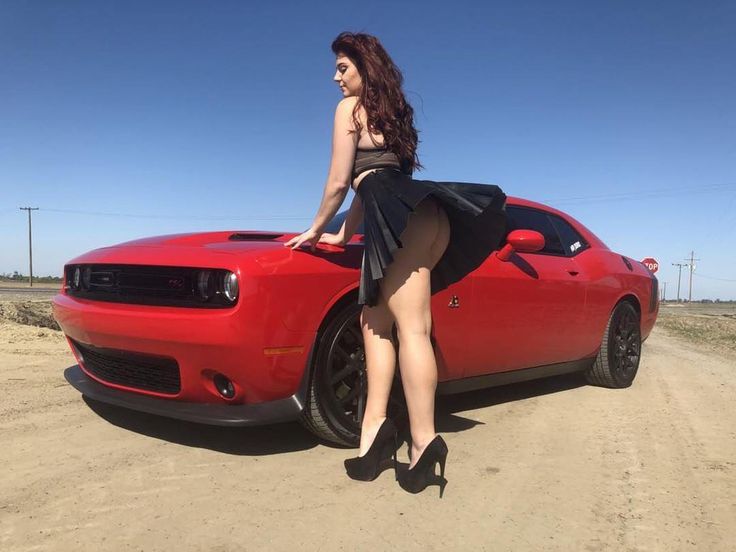 a woman leaning on the hood of a red sports car with her legs spread out