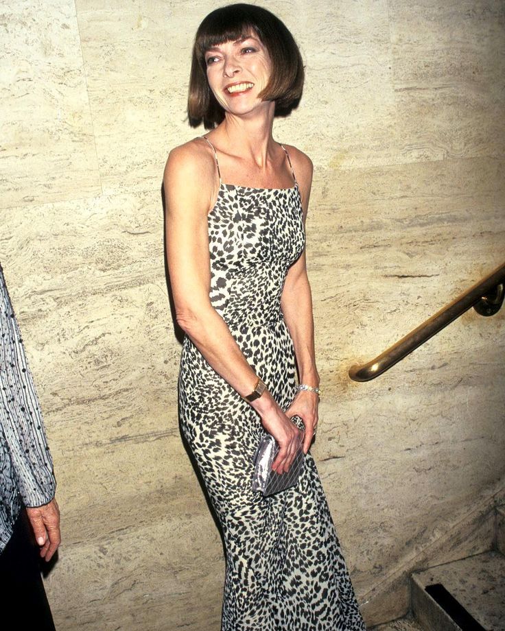 a woman in a leopard print dress standing next to a stair case and smiling at the camera