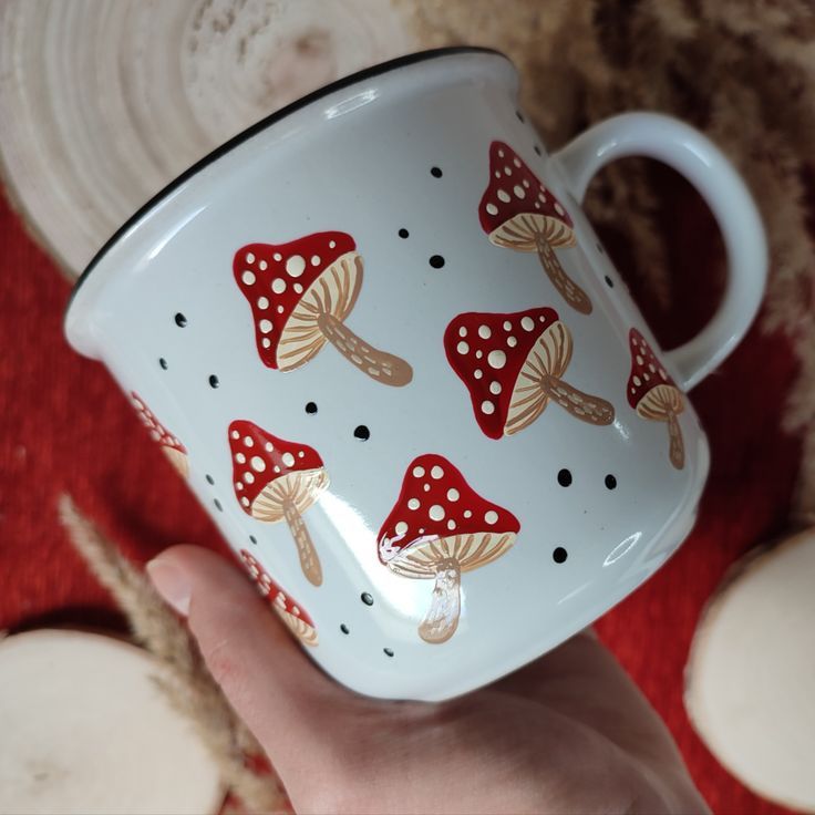 a hand holding a red and white coffee cup with mushrooms painted on the side,