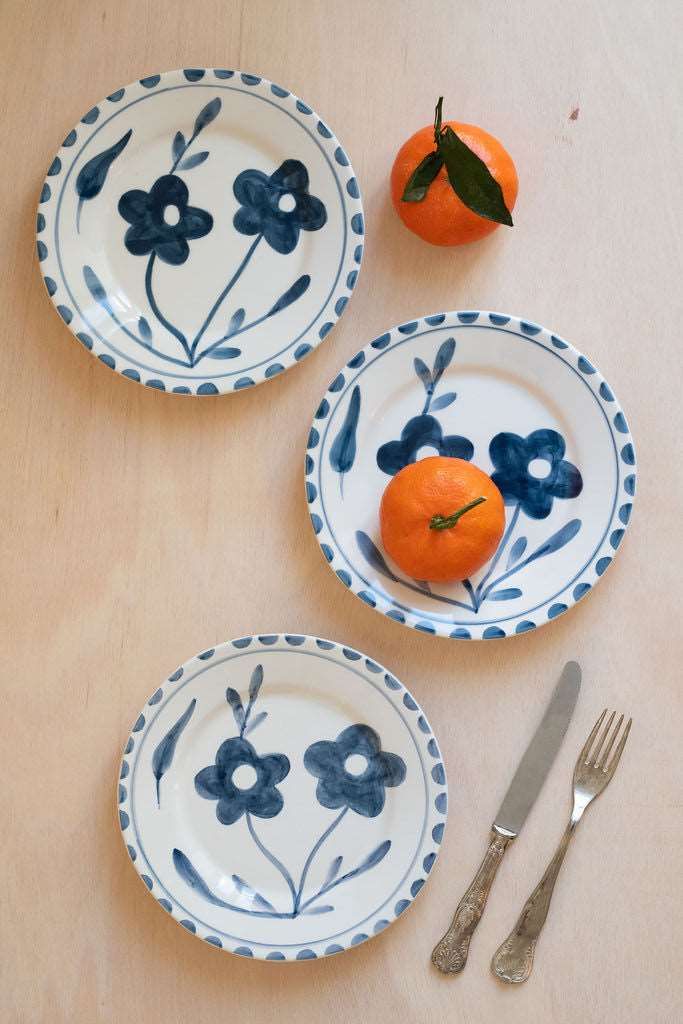 three blue and white plates with flowers on them next to an orange, fork and knife