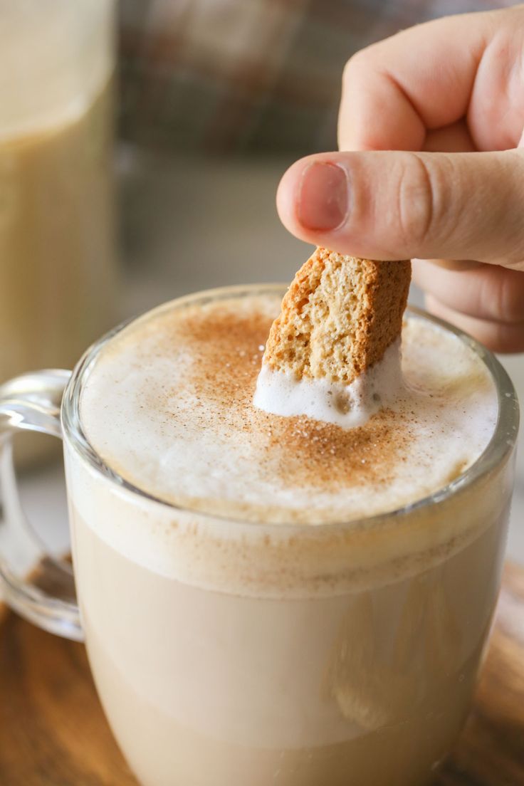 a person dipping a piece of food into a cup of coffee with milk in it