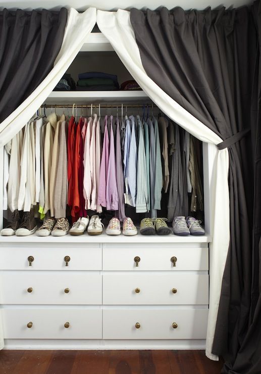 a white dresser topped with lots of clothes and shoes next to a black drapes