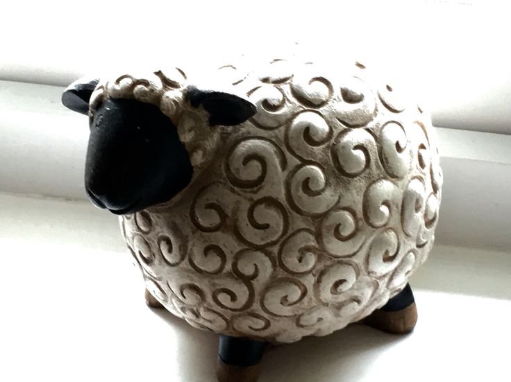 a ceramic sheep sitting on top of a window sill next to a white curtain