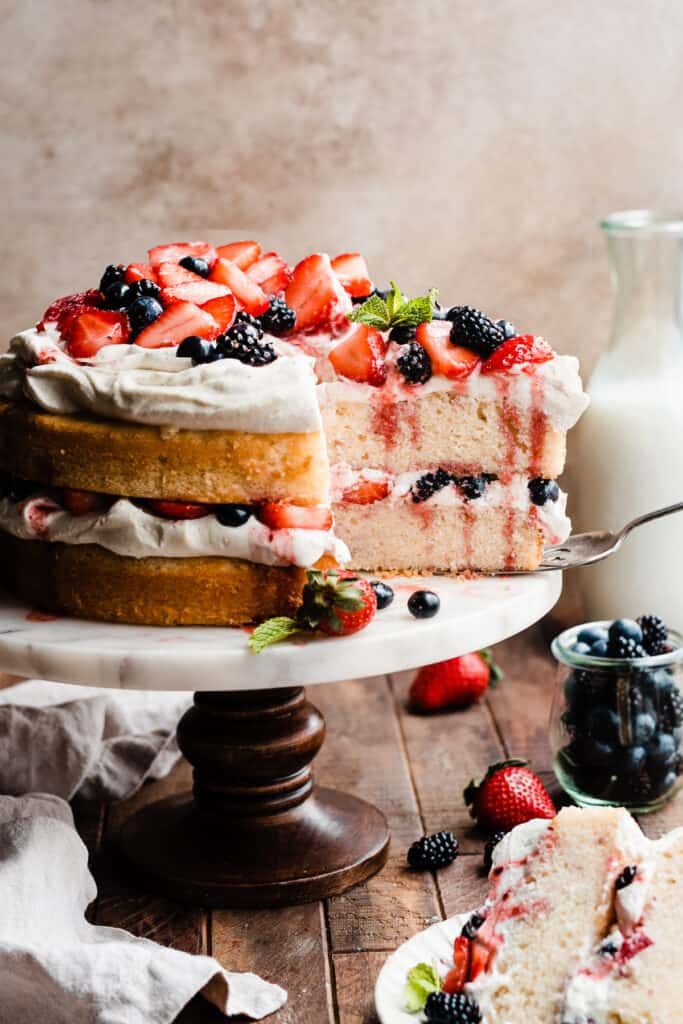 a cake with berries and whipped cream on top sitting on a wooden table next to a bottle of milk