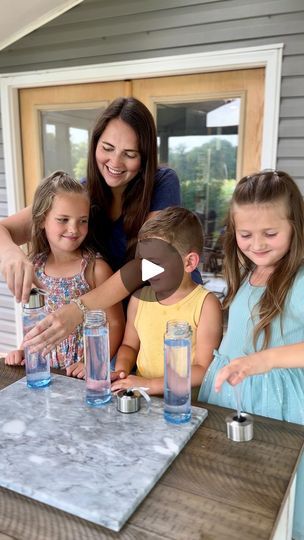 a group of children and an adult standing around a table with water bottles on it