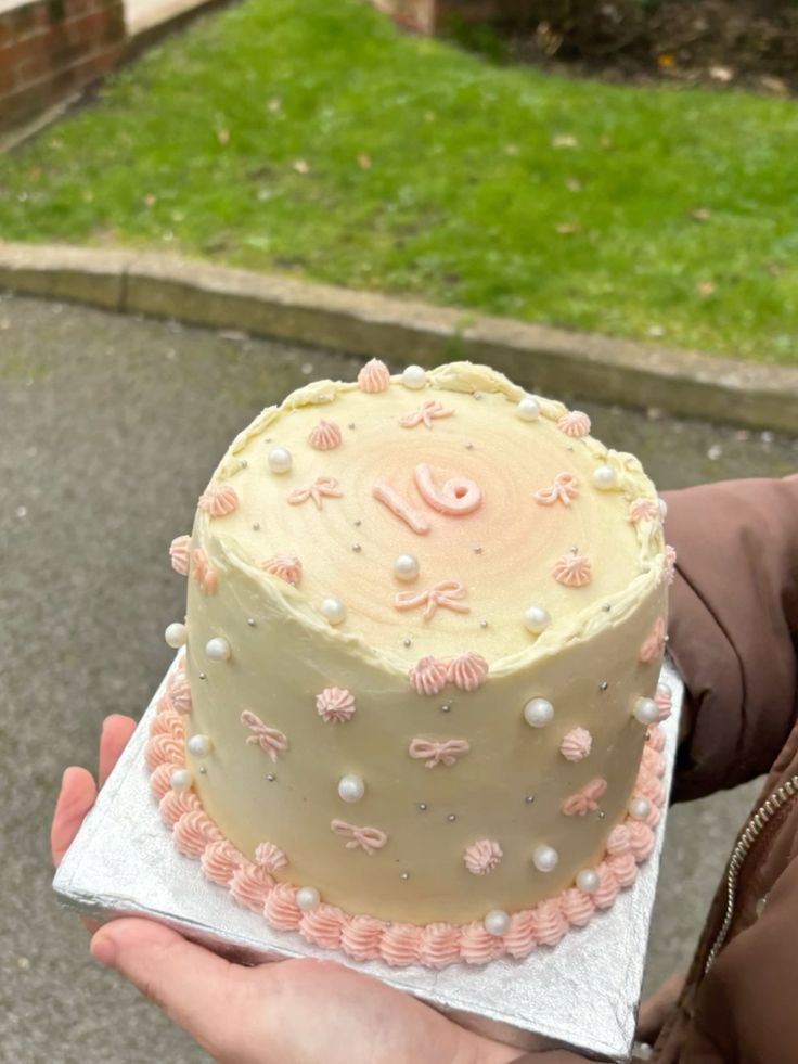 a person holding a cake in their hand on top of a sidewalk near some grass