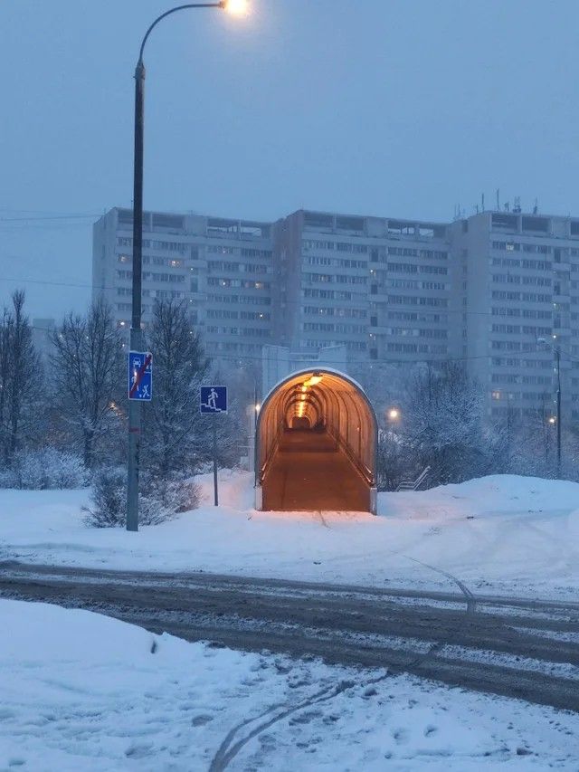 a tunnel in the middle of a snow covered road with buildings in the back ground