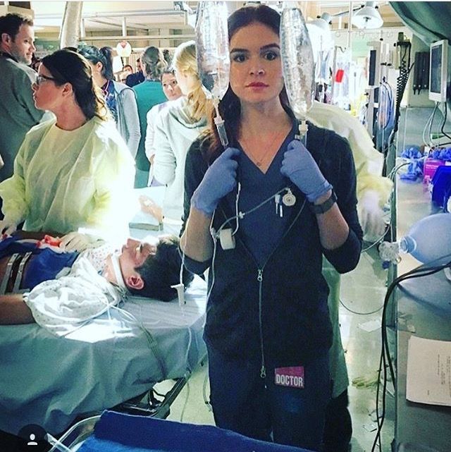 a woman in scrubs and gloves standing next to an operating room filled with people