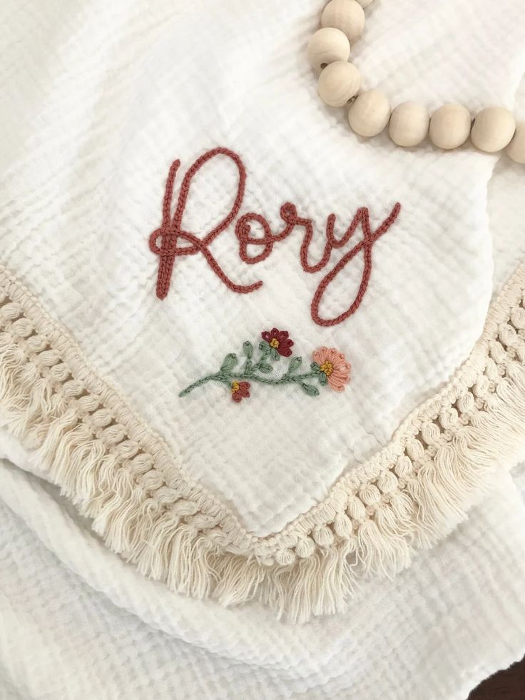 a white towel with the word rosy written on it and beads hanging from it's edge