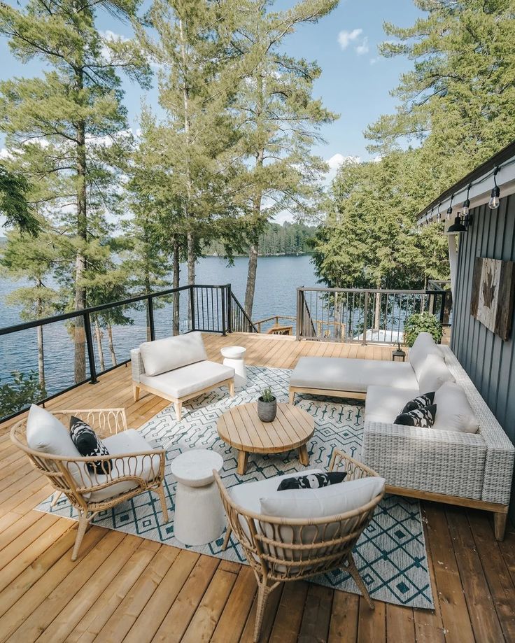 a deck with chairs and couches on it next to the water's edge