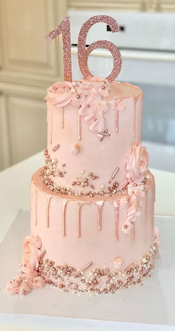 a pink birthday cake decorated with flowers and icing is displayed on a white table