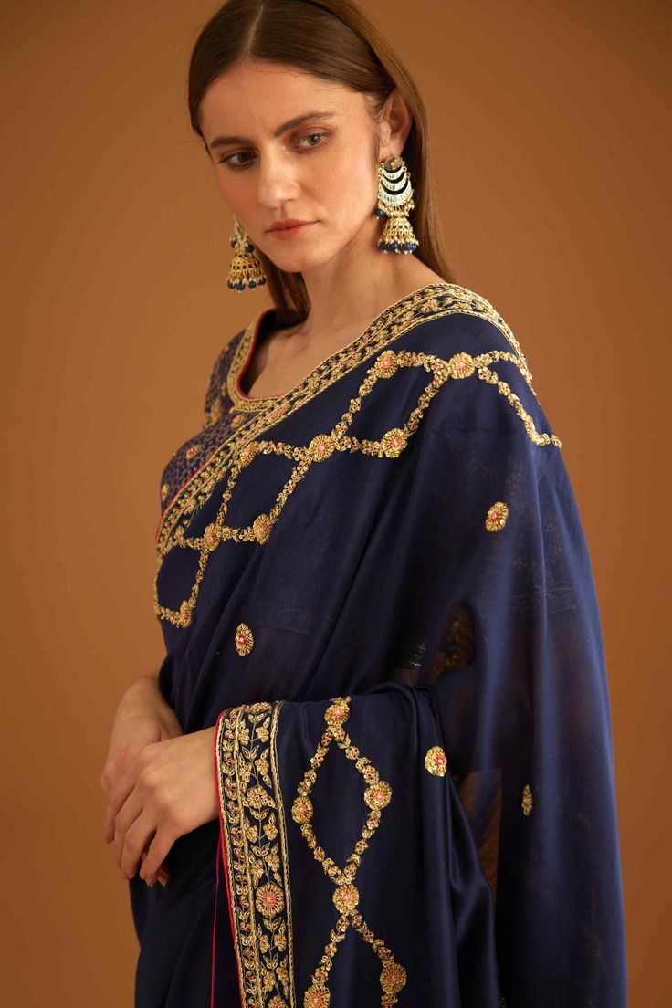 Editor's Note This set features a beautiful dark navy blue sari made of luxurious dupion silk. The sari is paired with a matching brocade blouse that has intricate embroidery work on it. The embroidery on the blouse is done with contrasting shades of blue and gold, creating a stunning visual appeal. The sari has a simple yet elegant look that complements the heavily embroidered blouse. The combination of the rich fabric and the intricate embroidery work makes this set perfect for any formal occa Traditional Blue Pre-draped Saree With Resham Embroidery, Festive Dola Silk Pre-draped Saree With Embroidered Border, Blue Bollywood Style Saree In Chinon, Blue Embroidered Pre-draped Saree For Transitional Season, Anarkali Choli With Embroidered Border In Dola Silk, Traditional Pre-draped Saree With Embroidered Border In Chinon, Navratri Art Silk Pre-draped Saree With Embroidered Border, Blue Traditional Pre-draped Saree With Intricate Embroidery, Bollywood Style Dola Silk Choli With Embroidered Border