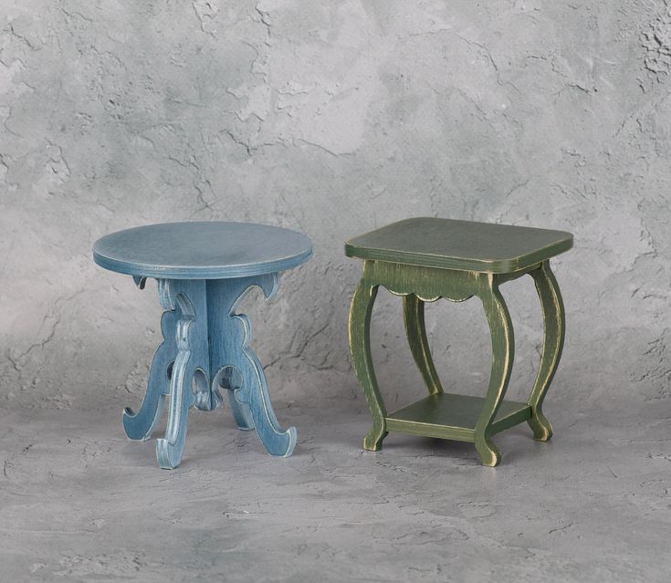 two small stools sitting next to each other in front of a gray wall and cement floor