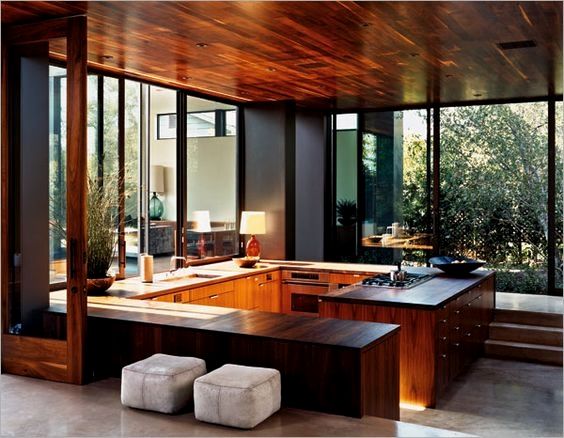 an open kitchen with wooden cabinets and counter tops in front of large glass windows that look out onto the backyard