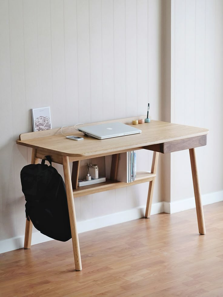 a laptop computer sitting on top of a wooden desk next to a book case and backpack