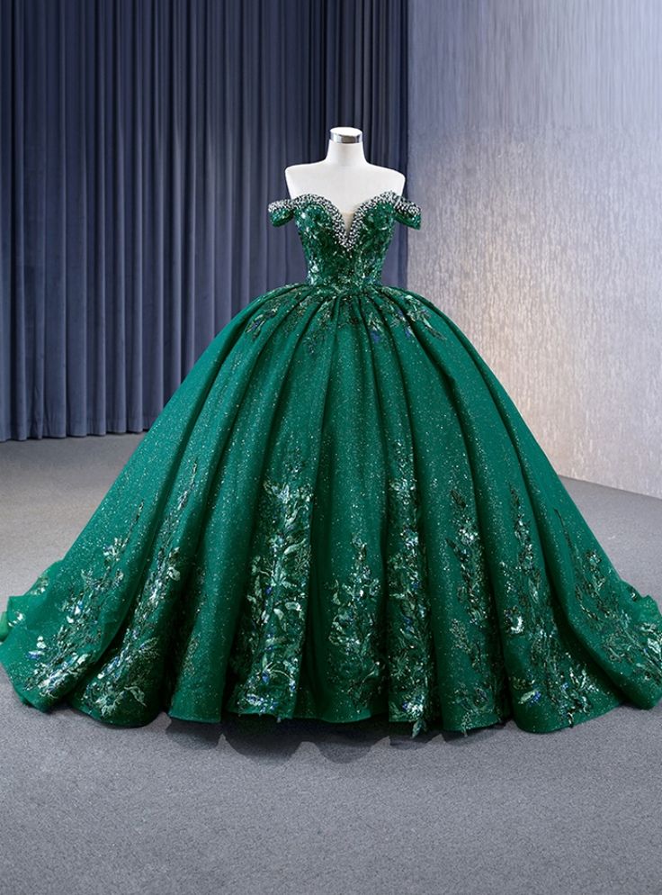 Daringly enchanting, this prom dress is designed to captivate and mesmerize. The rich emerald green hue, adorned with glittering accents, evokes the enchanting beauty of a lush, magical forest. The off-the-shoulder bodice is intricately embellished with sparkling details, highlighting your neckline and shoulders with a touch of elegance and sophistication. The voluminous skirt flows gracefully to the floor, creating a dramatic and regal silhouette. As you move, the shimmering fabric catches the light, creating a magical effect that will captivate everyone around you. Imagine making your grand entrance in this gown, the layers of the skirt swaying with each step, exuding grace and confidence. This dress is perfect for those who want to combine timeless elegance with a hint of modern glamour 15 Dresses Quinceanera Emerald Green, Dark Forest Green Quinceanera Dress, Forest Green Ball Gown, Emerald Green 15 Dress, Dark Green Wedding Dress, Emerald Quinceanera Dress, Emerald Green Quince Dress, Emerald Green Wedding Dress, Emerald Green Quinceanera Dresses