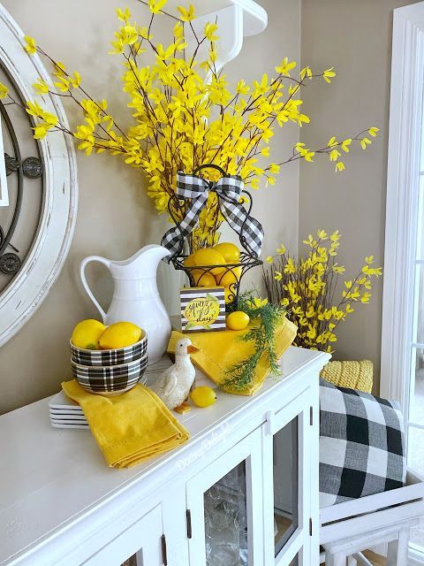 a white mantle with yellow flowers, lemons and dishes on it next to a clock