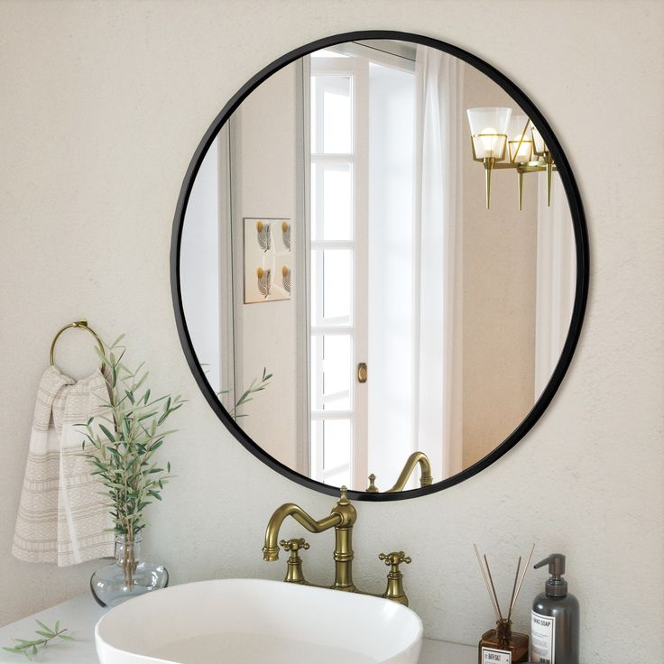 a bathroom sink under a round mirror in front of a window with plants on the counter