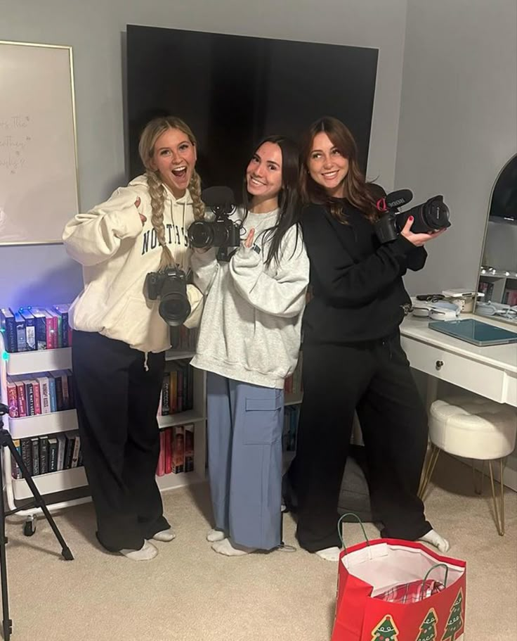 three women standing in front of a mirror holding up their camera's hands and taking pictures