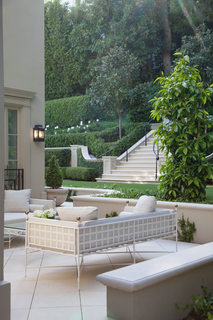 an outdoor seating area with white furniture and greenery in the background, surrounded by trees