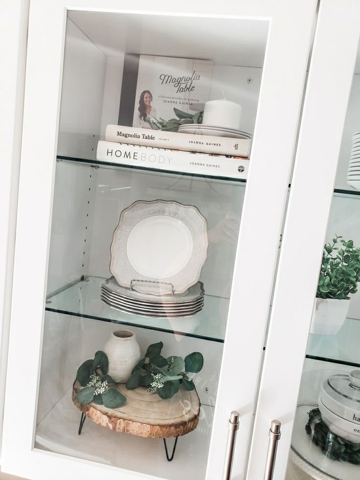 a white china cabinet with glass shelves filled with plates and other items on top of it