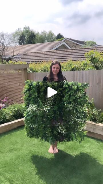 a woman holding up a fake tree in her backyard