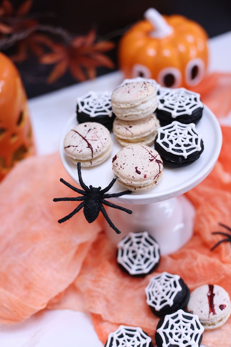 halloween cookies on a white plate with spider web decorations and fake pumpkins in the background