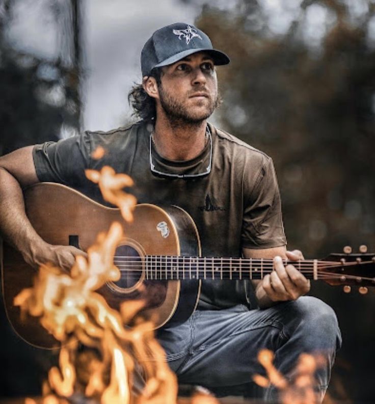 a man sitting in front of a fire holding a guitar