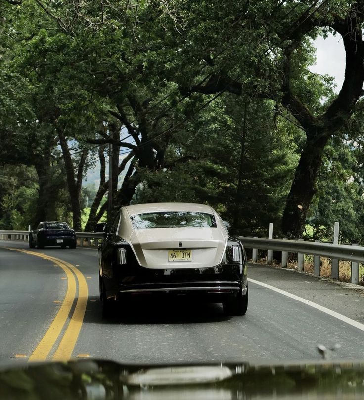 a car driving down the road with trees in the back ground and another car behind it