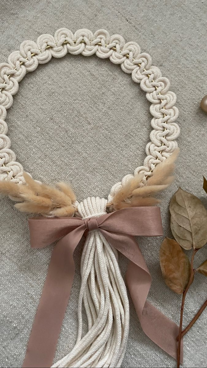 a white necklace with a pink ribbon tied to it and some leaves on the ground